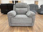 Gray recliner chair in a showroom setting with other furniture in the background.